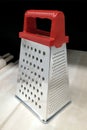 A nickel-plated grater for vegetables and cheese with a red handle standing