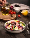 Nicoise salad with tuna, egg, olives and lettuce leaves on a wooden table. A man& x27;s hand holds a small jug of olive Royalty Free Stock Photo