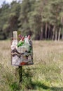 A metal litter bin full with rubbish on a wooden post in the countryside