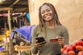 nigerian lady selling in a local nigerian market using her mobile phone and credit card to do a transaction online smiling Royalty Free Stock Photo