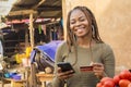 nigerian lady selling in a local nigerian market using her phone and credit card to do a transaction online smiling Royalty Free Stock Photo