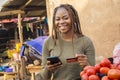 nigerian woman selling in a local nigerian market using her mobile phone and credit card to do a transaction online smiling Royalty Free Stock Photo