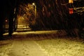 Night alley, snowfall in the light of a street lamp, glowing windows of the house, gloomy mood traces in the snow of the alley,