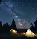 Night camp with burning bonfire and two tents in pine forest under bright starry sky on which the Milky Way Royalty Free Stock Photo