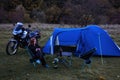 Night camp on the wilderness. Camping with big blue tent and touring motorcycle, Woman is sitting on folding chairs use smatphone Royalty Free Stock Photo