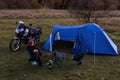 Night camp on the wilderness. Camping with big blue tent and touring motorcycle, Woman is sitting on folding chairs use smatphone Royalty Free Stock Photo