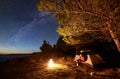 Woman having a rest at night camping near tourist tent, campfire on sea shore under starry sky Royalty Free Stock Photo