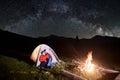 Couple tourists near campfire and tents under night sky full of stars and milky way Royalty Free Stock Photo