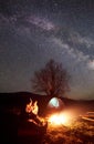 Night camping in mountains. Couple hikers having rest near campfire, tourist tent under starry sky Royalty Free Stock Photo