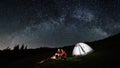 Couple tourists near campfire and tents under night sky full of stars and milky way Royalty Free Stock Photo