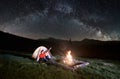 Couple tourists near campfire and tents under night sky full of stars and milky way