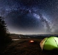 Night camping in the mountains. Illuminated tent and campfire under night sky full of stars and milky way Royalty Free Stock Photo