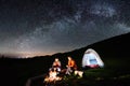 Couple tourists near campfire and tents under night sky full of stars and milky way Royalty Free Stock Photo