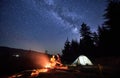 Night camping in mountains near forest with campfire and tourist tent. Royalty Free Stock Photo