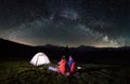 Couple tourists near campfire and tents under night sky full of stars and milky way Royalty Free Stock Photo