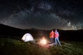 Couple tourists near campfire and tents under night sky full of stars and milky way Royalty Free Stock Photo