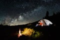 Couple tourists near campfire and tents under night sky full of stars and milky way Royalty Free Stock Photo