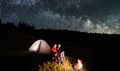 Couple tourists near campfire and tents under night sky full of stars and milky way Royalty Free Stock Photo