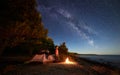 Woman having a rest at night camping near tourist tent, campfire on sea shore under starry sky Royalty Free Stock Photo