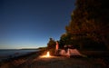 Woman having a rest at night camping near tourist tent, campfire on sea shore under starry sky Royalty Free Stock Photo