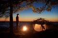 Woman having a rest at night camping near tourist tent, campfire on sea shore under starry sky Royalty Free Stock Photo