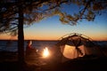 Woman having a rest at night camping near tourist tent, campfire on sea shore under starry sky Royalty Free Stock Photo