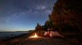 Woman having a rest at night camping near tourist tent, campfire on sea shore under starry sky Royalty Free Stock Photo