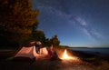 Woman having a rest at night camping near tourist tent, campfire on sea shore under starry sky Royalty Free Stock Photo