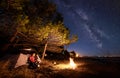 Woman having a rest at night camping near tourist tent, campfire on sea shore under starry sky Royalty Free Stock Photo