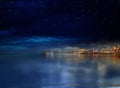 Night city blurred light on horizon at sea blue water wave starry sky
