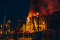Night fire in apartment building, firefighters struggle with flame, people stand around. Fire disaster and accident tragedy