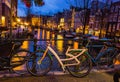 Night illumination of Amsterdam canal and bridge with typical dutch houses, boats and bicycles. Royalty Free Stock Photo