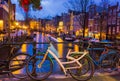 Night illumination of Amsterdam canal and bridge with typical dutch houses, boats and bicycles. Royalty Free Stock Photo