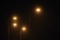 Night lamppost shines with faint mysterious yellow light through evening fog at quiet city night