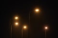 Night lamppost shines with faint mysterious yellow light through evening fog at quiet city night