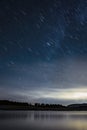 Night landscape with a sky with stars trail, with the silhouette of a forest in the background and a lake in the foreground