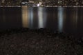 Night lights reflected in the water, stones on the shore Royalty Free Stock Photo