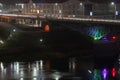 Night panorama of the big city at the foot of the river. Lots of colorful burning lights and street lighting. Top view of houses