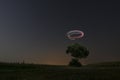 Night photo outdoors. There is a tree in the meadow above which the drone circles. The long shutter speed photo contains grains. Royalty Free Stock Photo