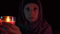 A night portrait of a witch casting spell over a red candle and making witchcraft, she moves a candle close up to the camera and