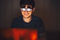 Night portrait of young happy man wearing round glasses, looking in laptop in dark room with garlands at home. Royalty Free Stock Photo