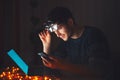 Night portrait of young man wearing round glasses using laptop and smartphone in dark room at home. Royalty Free Stock Photo