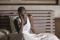 Night portrait of young scared and stressed black afro American woman on bed upset unable to sleep suffering hangover headache and