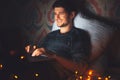 Night portrait of young smiling man lying on pillow on bed with laptop in dark room at home with garlands. Royalty Free Stock Photo