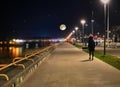 night promenade at sea side blue starry sky and full moon street lantern blurred light at sea water people silhouette walk an