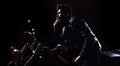 Night racer concept. Man with beard, biker in leather jacket sitting on motor bike in darkness, black background. Macho