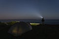 Night scene, camping site, a man with a headlamp stands on a cliff by the sea in the background is a tent Royalty Free Stock Photo