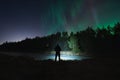 Night scene, nature of Estonia. Silhouette of a man with a flashlight in a dark forest with a starry sky and northern lights Royalty Free Stock Photo