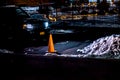 Night scene of parked car with headlights illuminating orange cone and a pile of snow. Royalty Free Stock Photo