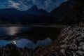 Night scene in the Swiss Alps. The calm water of a small mountain lake reflects the light of the moon, which blends in with the Royalty Free Stock Photo